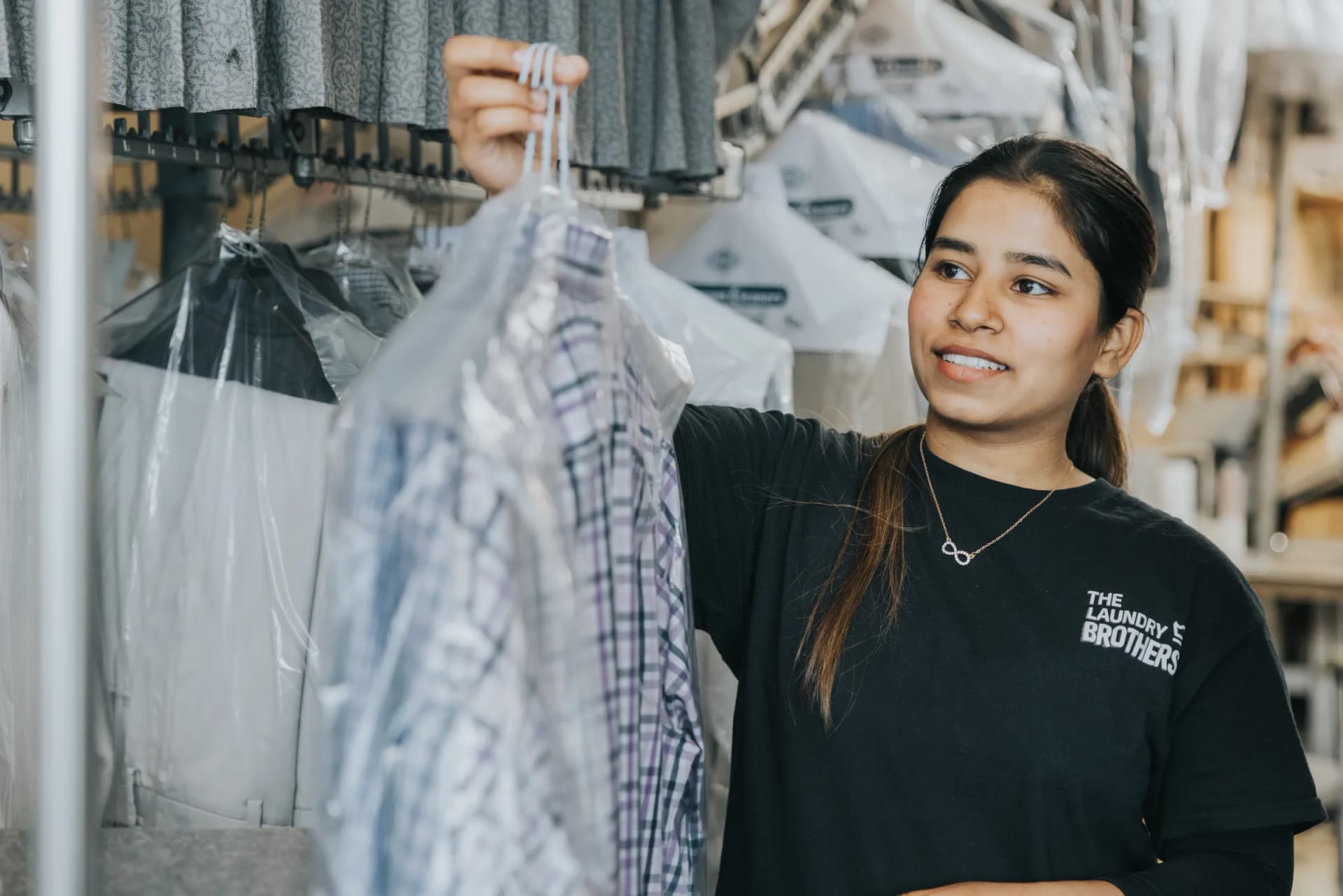 A Laundry Brothers team member smiling while pulling a freshly pressed garment from the dry cleaning rack.